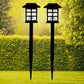 A pair of sleek black solar garden lights illuminating a lush green lawn at dusk.