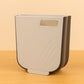 Collapsible hanging trash can mounted on a kitchen cabinet door, collecting food waste.