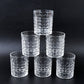 Three diamond-cut glass tumblers filled with different beverages on a wooden surface, ready for serving.