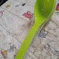 Single black plastic kitchen ladle resting on a rustic wooden table, ready for use.