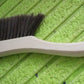 Hand holding a soft bristle brush, gently cleaning a sofa surface to remove dust.