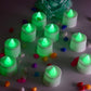 Green flameless LED tealights glowing softly on a dark surface.
