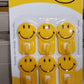A yellow smiley face adhesive hook against a white background, ready for use.