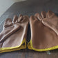 Close-up of a gardener's hand wearing a BraveVault leather glove, holding a small garden tool.