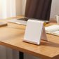 White foldable mobile phone holder positioned on a wooden desk