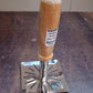 Stainless steel potato masher with wooden handle hanging on kitchen rack