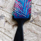 Packaging for the ergonomic hair brush alongside the product, ready for use.