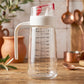 Glass oil dispenser bottle with auto-flip cap, side handle, and measurement scale for precise kitchen pouring